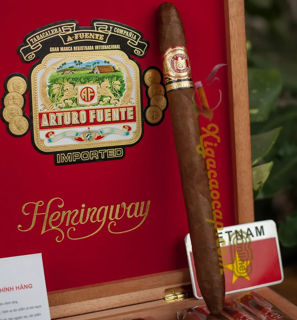 Xì gà Arturo Fuente Hemingway Masterpiece đặt cạnh logo thương hiệu Fuente bên trong hộp